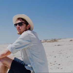 Contemplating on the beach with his sunglasses on and a panama hat on his head