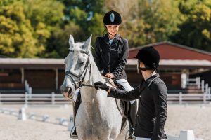 male equestrians holding horse halter, female jockey sitting on horse at horse club
