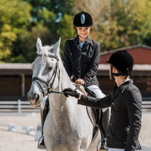 male equestrians holding horse halter, female jockey sitting on horse at horse club
